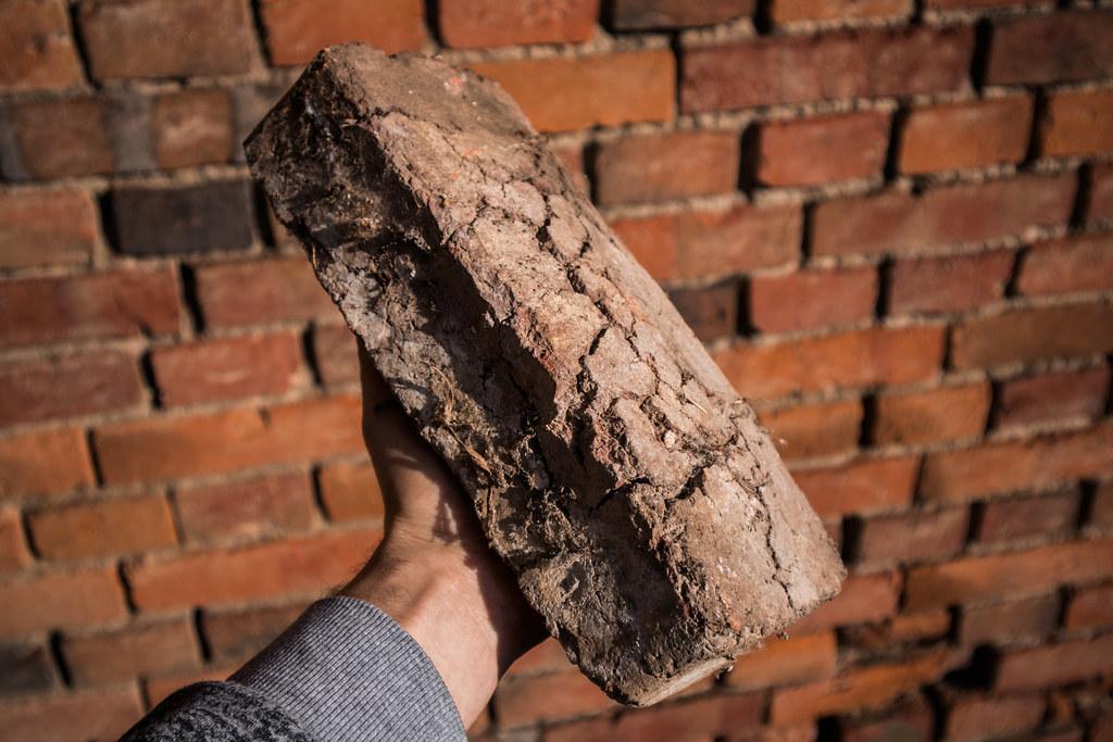 Man holding a bloated and cracked brick unusable for construction work by Ivan Radic holding brick photo