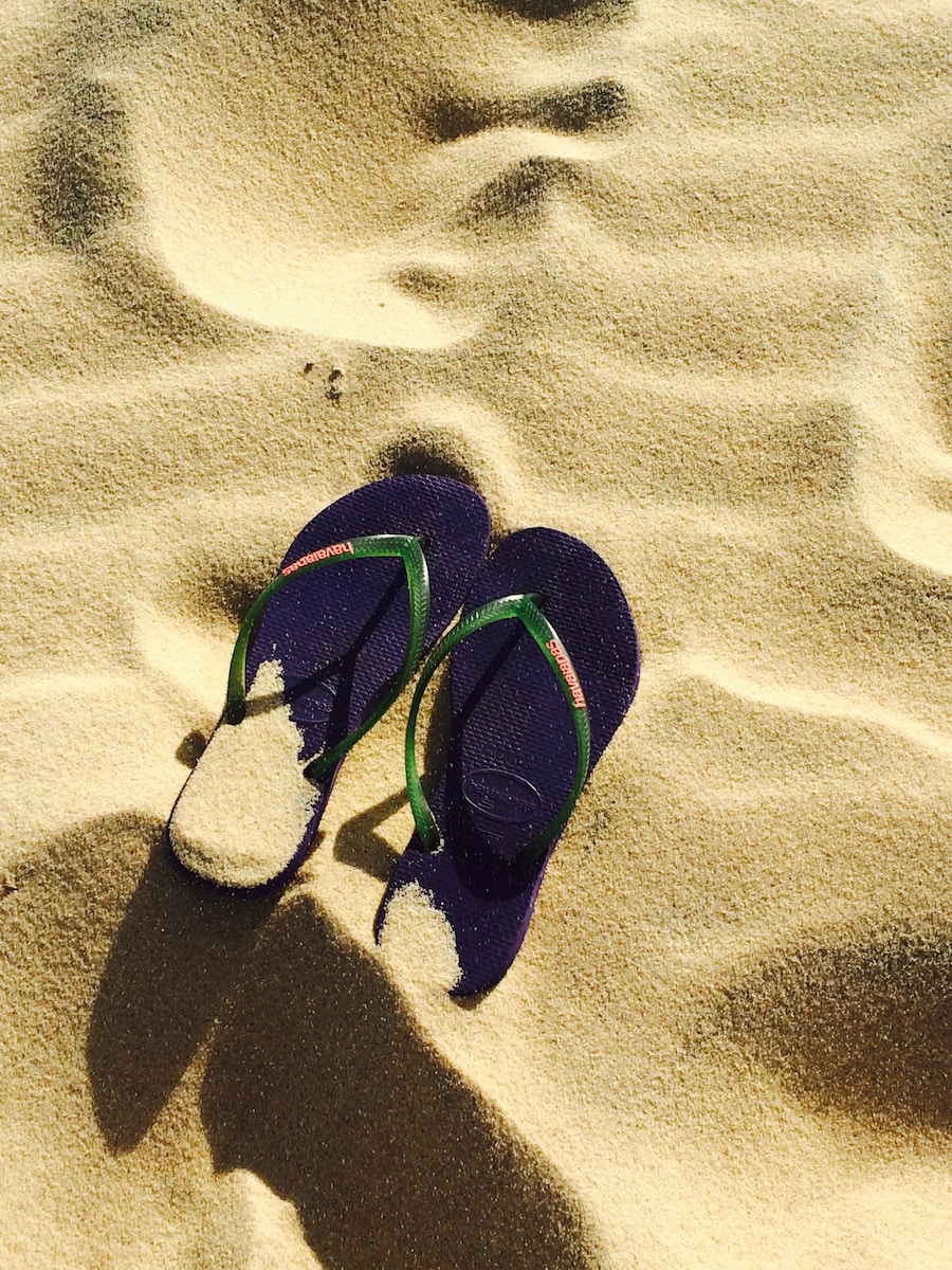 black and green flip flops on sand