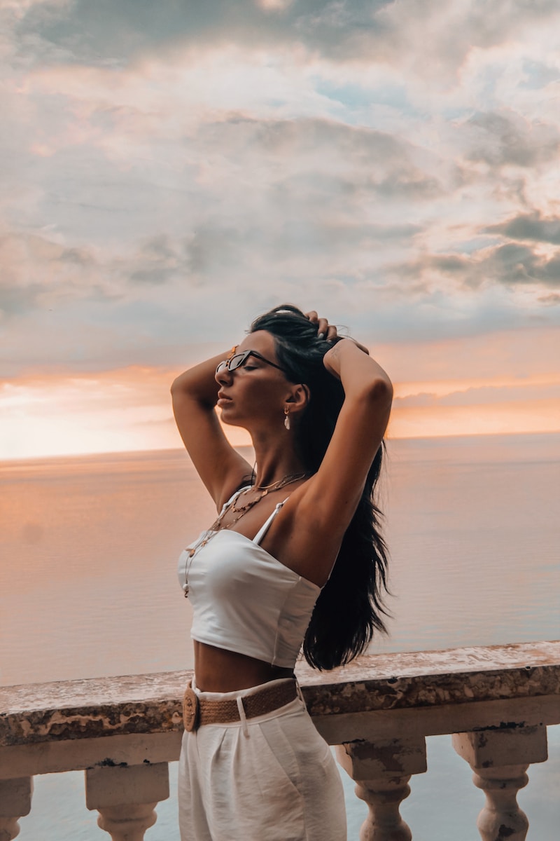 woman in white tank top and blue denim shorts standing on beach shore during sunset