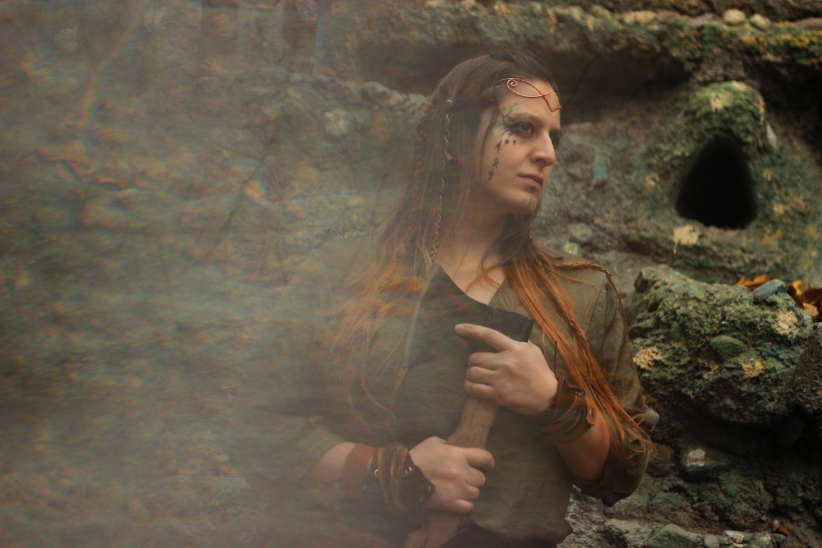 a woman dressed in costume standing in front of a cave
