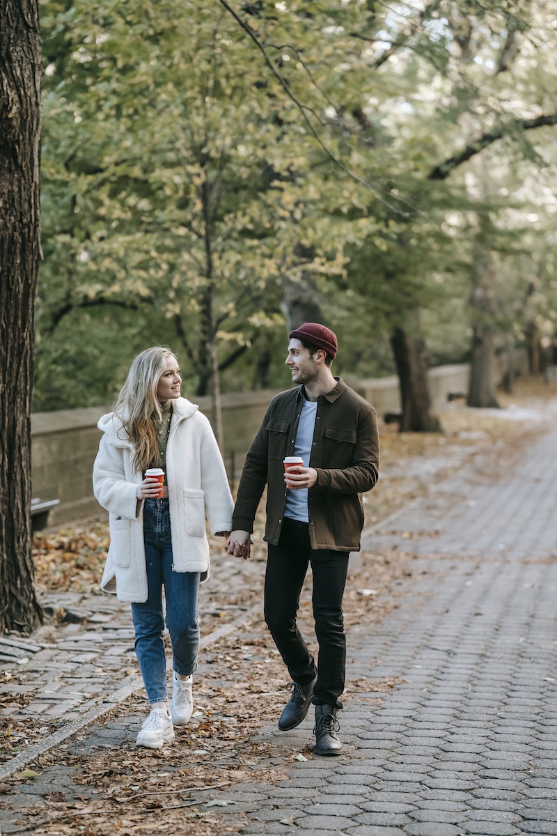 Young couple strolling and chatting in park with coffee cups