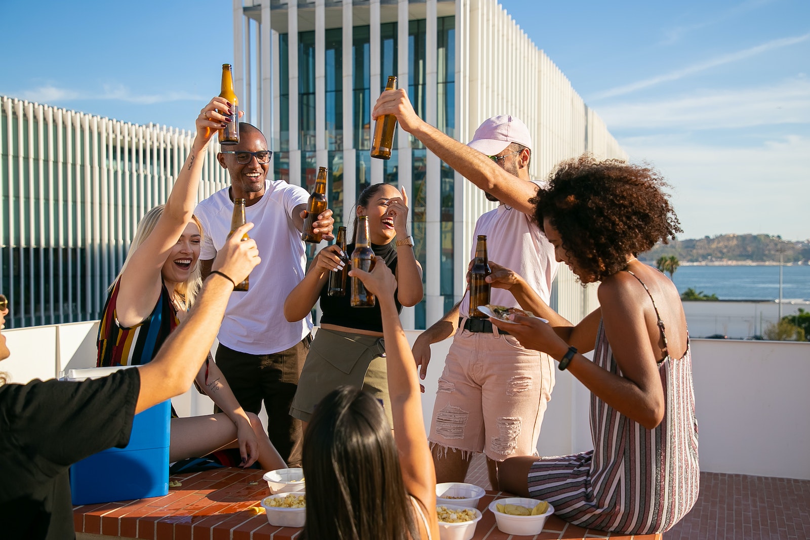 Joyful diverse friends toasting with beer bottles on rooftop