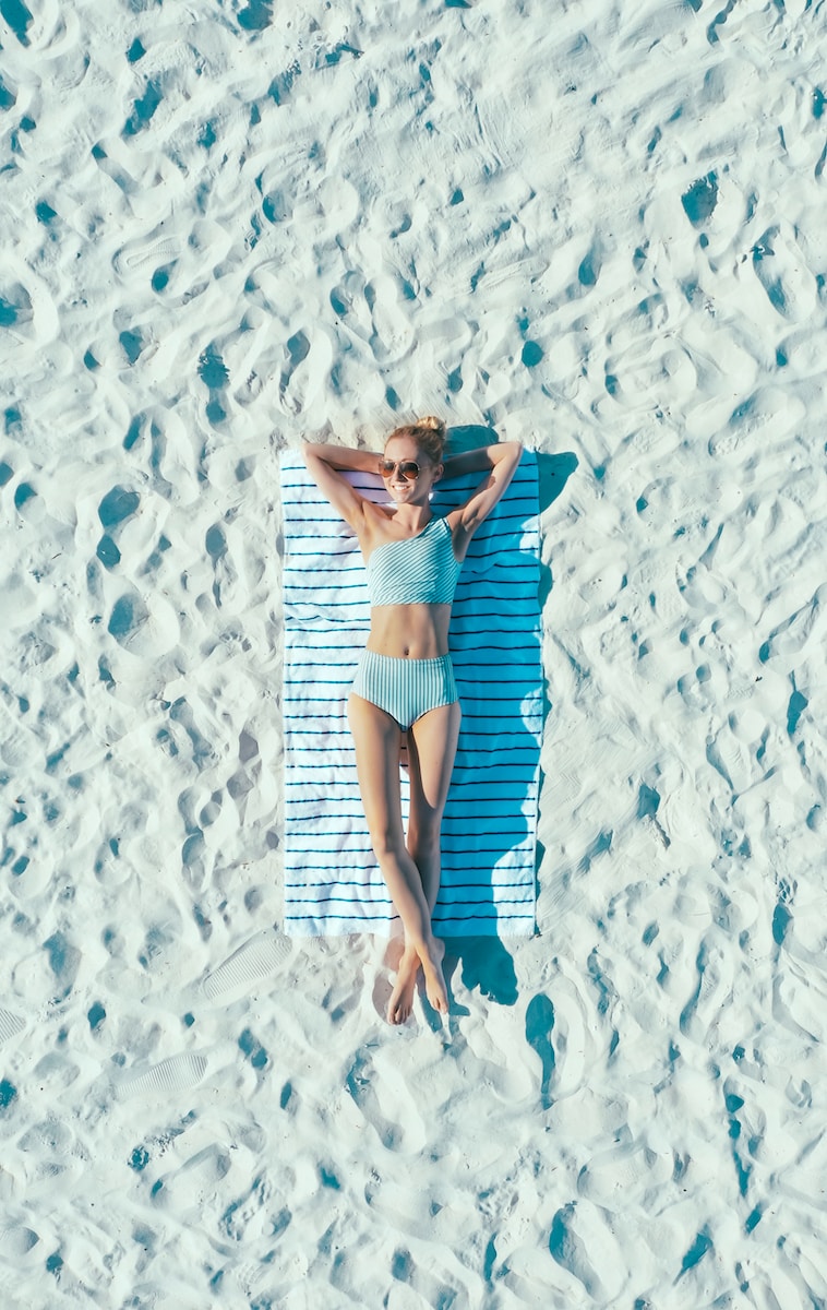 woman lying on sand with towel during daytime