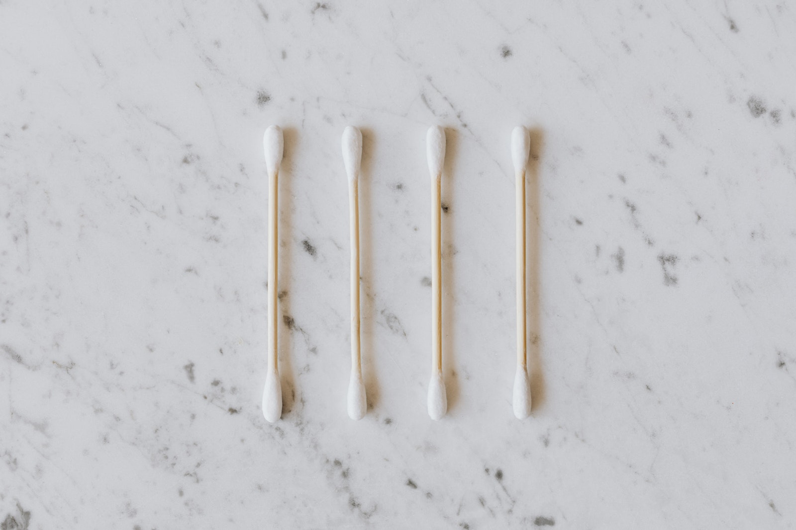 Top view of identical cotton swabs on thin wooden sticks with soft rounded edges on marble surface with tiny spots and gray lines