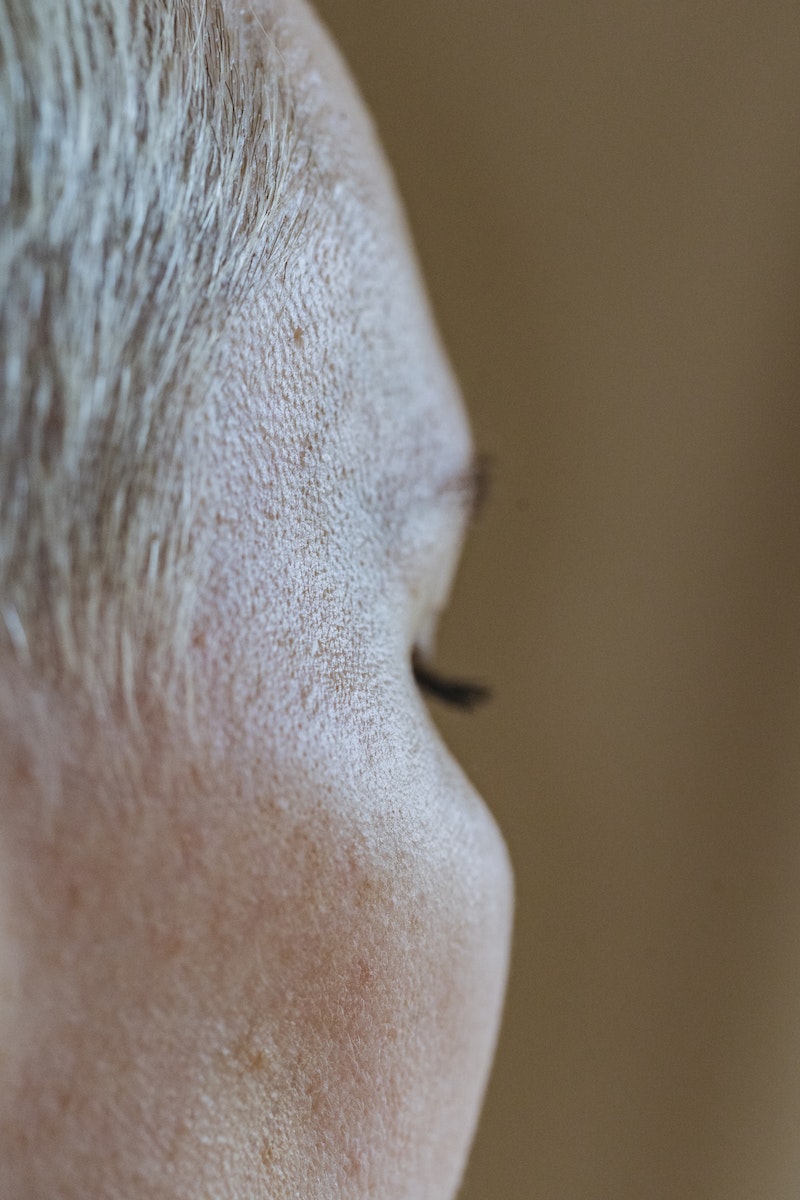 Closeup of crop unrecognizable female with short blond hair and freckles on face against blurred brown background