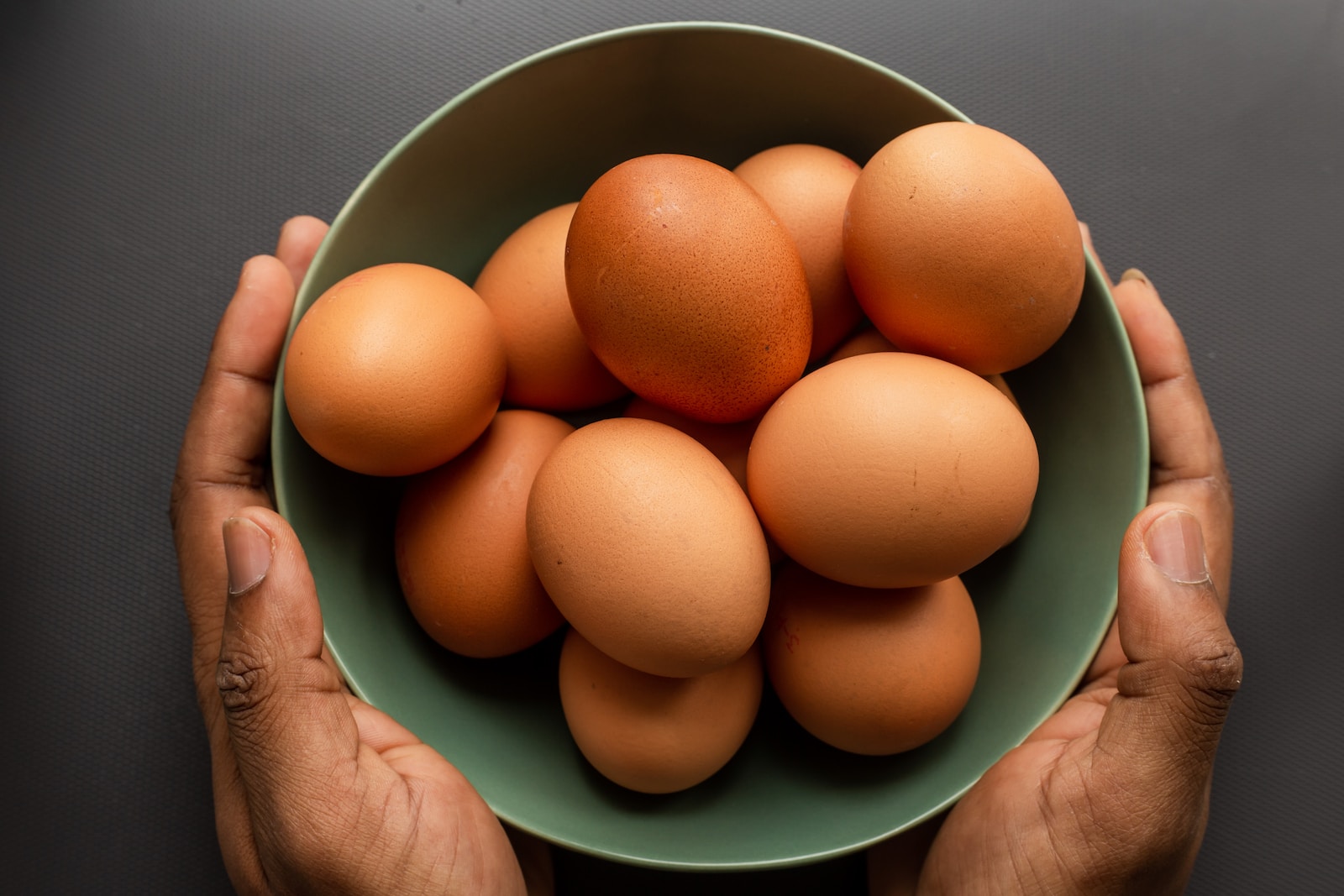 person holding brown egg on green ceramic bowl