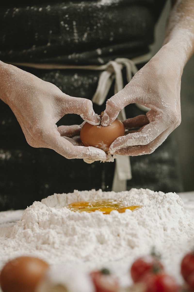 Crop cook breaking egg into flour