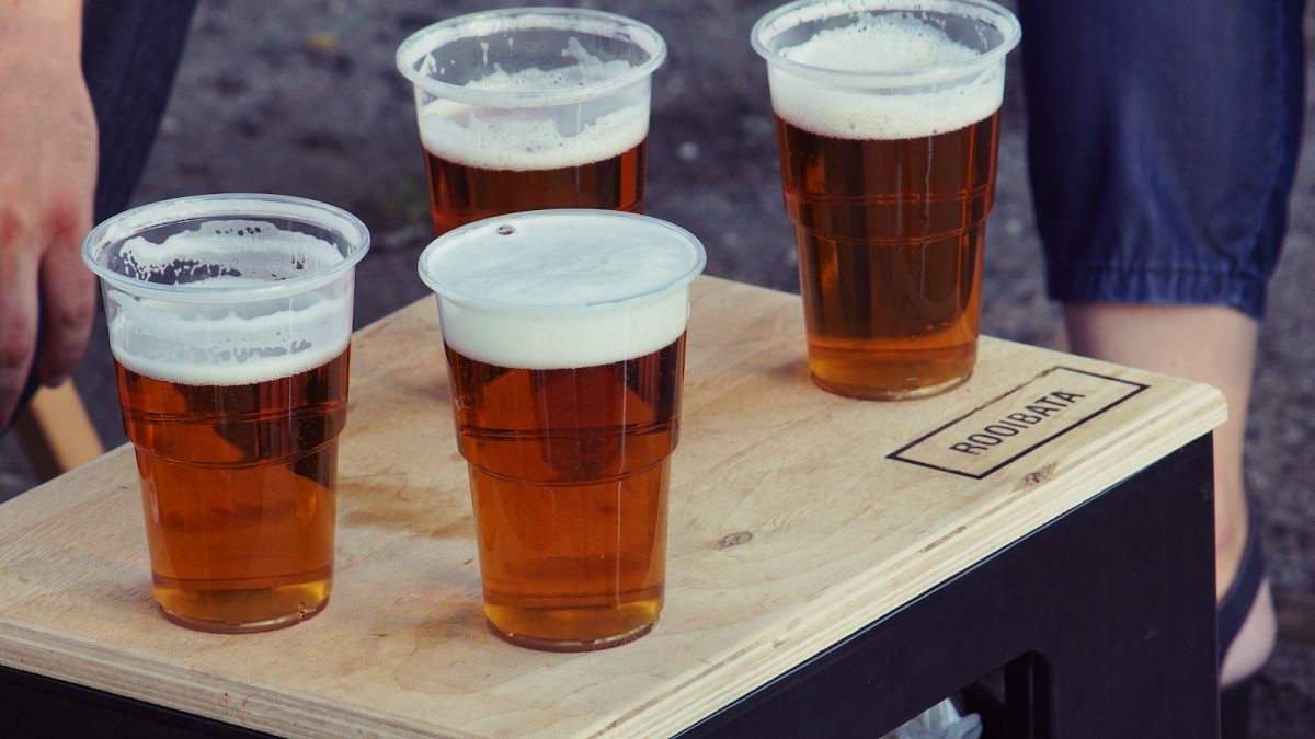 four clear plastic disposable cups with beer on the top of the board