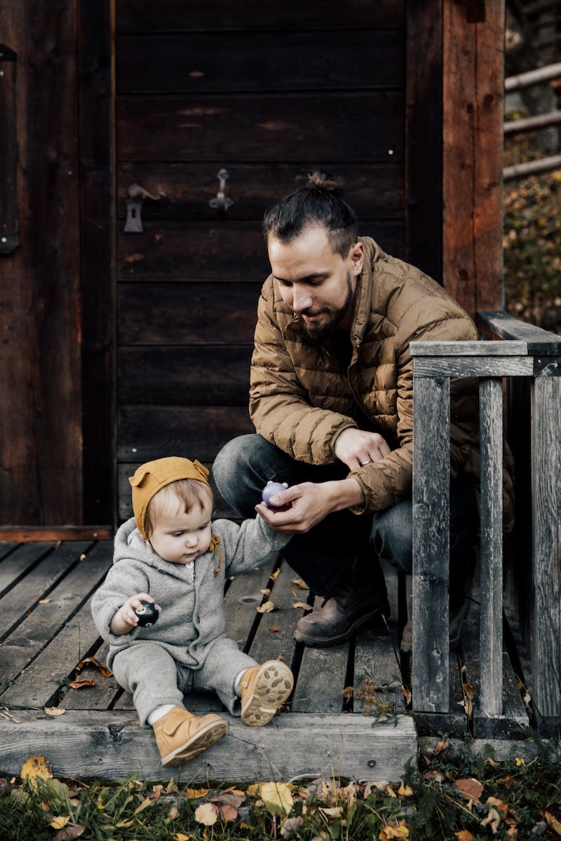 Man in Brown Jacket and Blue Denim Jeans Sitting Holding His Child