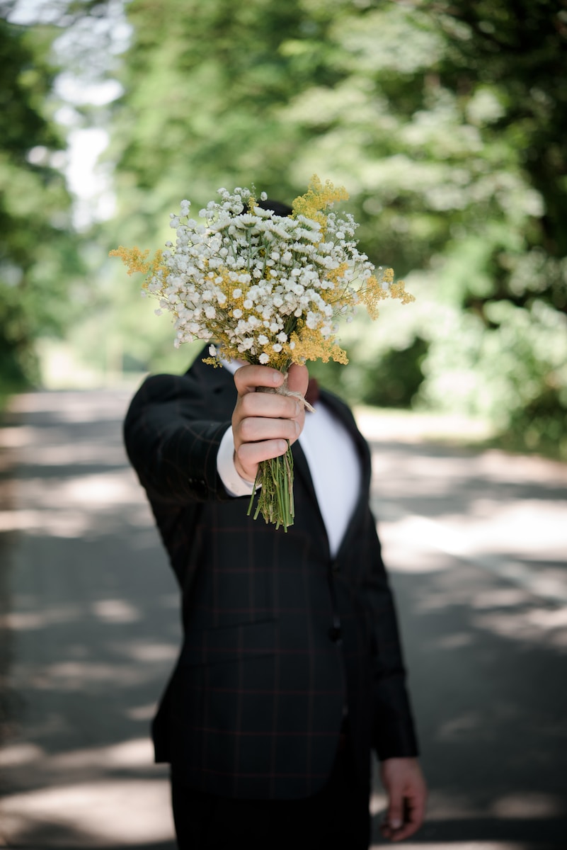 selective focus photo of man wearing black suit jacket holding flower bouquet