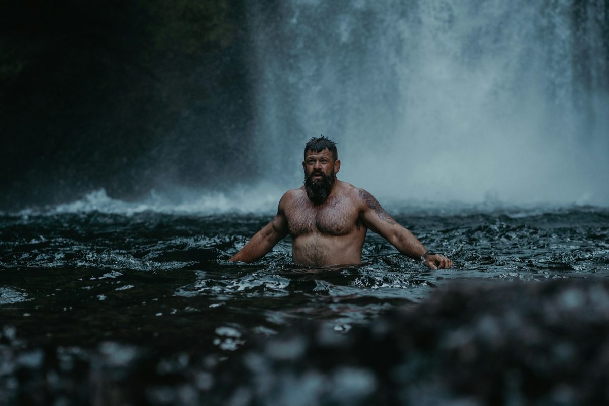 a man standing in the water in front of a waterfall