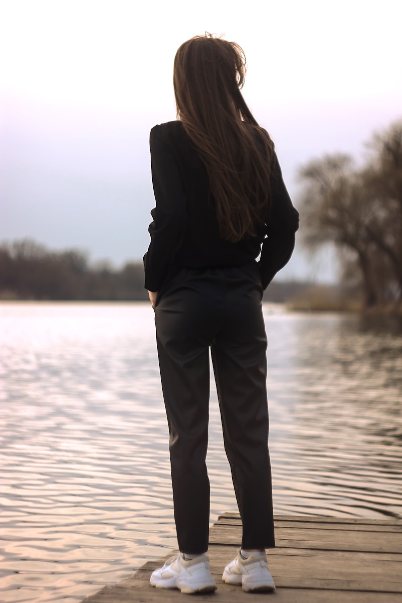 woman in black coat standing on brown wooden dock during daytime