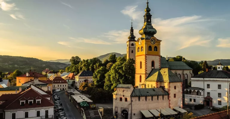 Historické centrum s vežou a horami v pozadí pri západe slnka, pokojná atmosféra Banskej Bystrice v prírode.