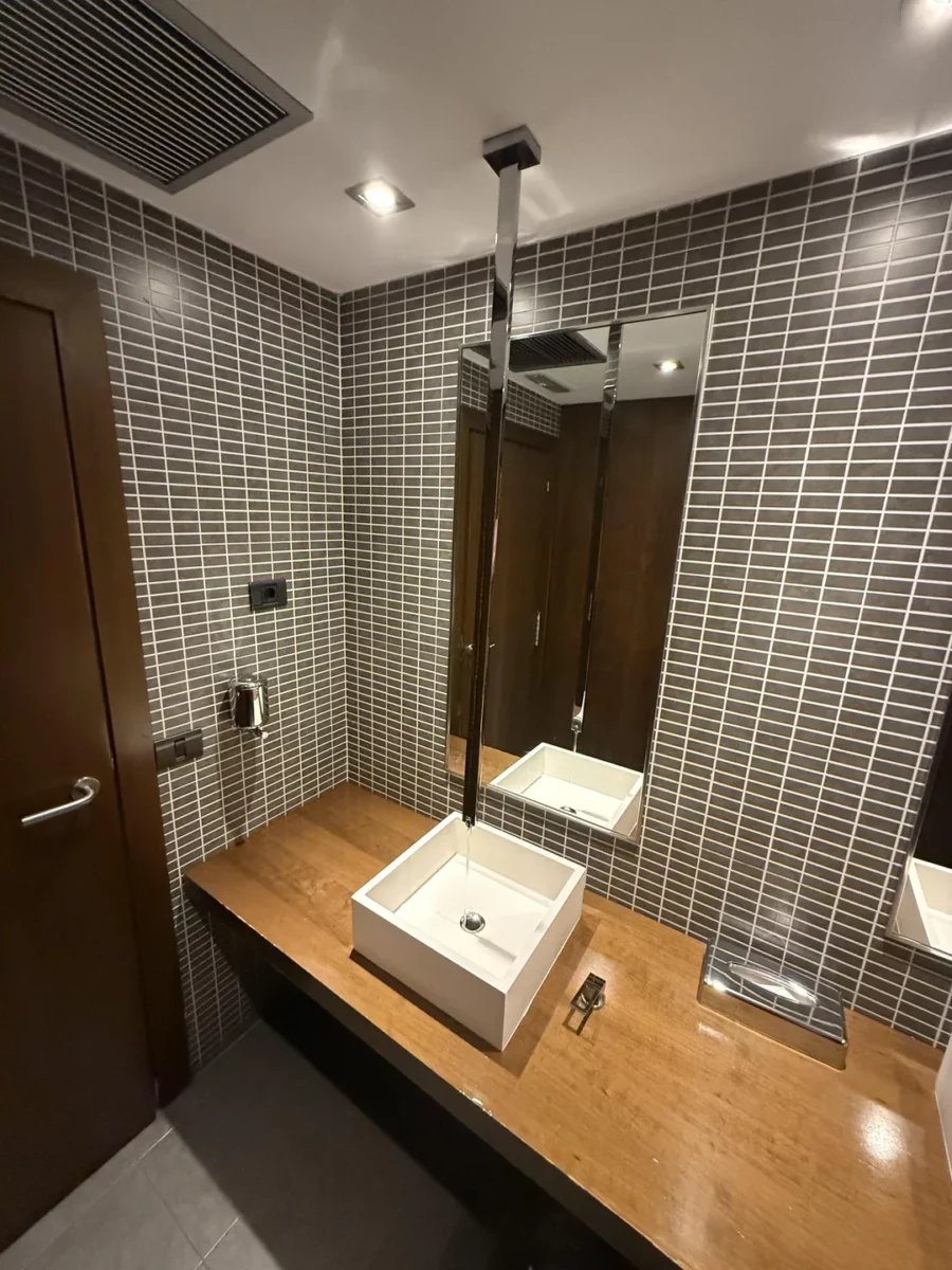 Moderná kúpeľňa s umývadlom na drevenej doske a obkladom zo sivých dlaždíc.