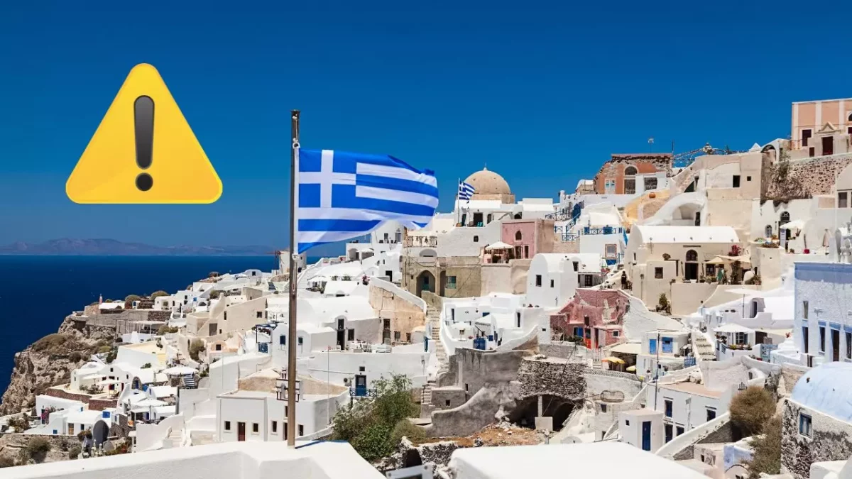 Grécka vlajka veje nad bielymi domami ostrova Santorini, na oblohe výstražný symbol.