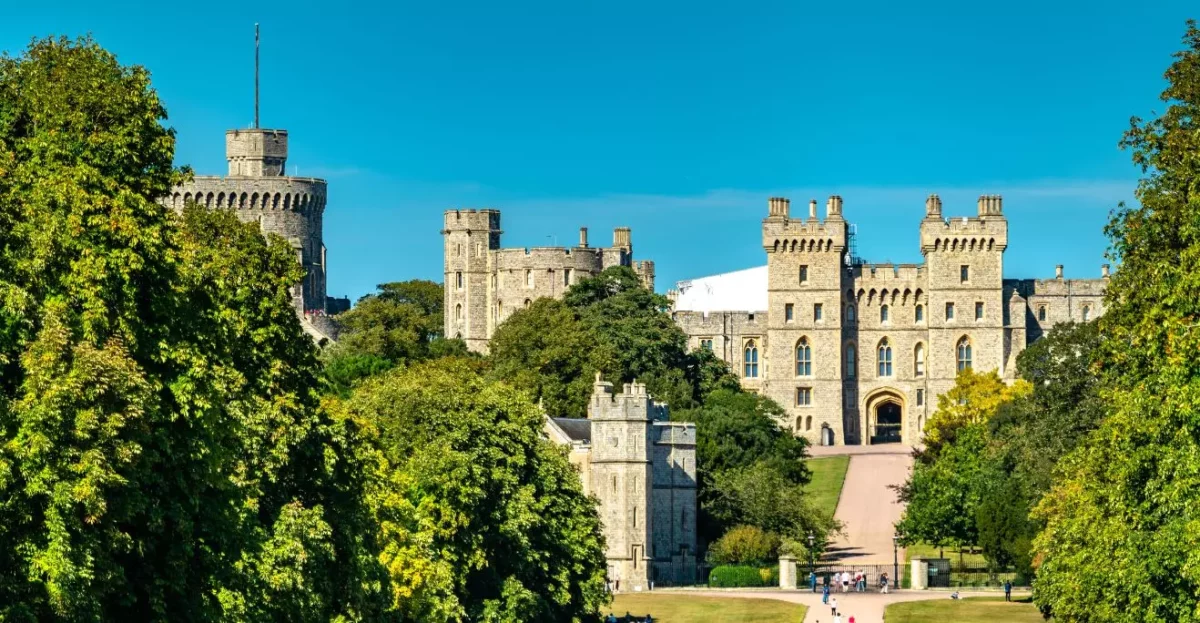 Historický hrad obklopený zeleňou so slnečnou oblohou na pozadí.