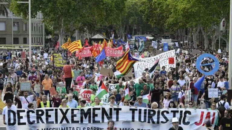 Demonštrácia v Barcelone za obmedzenie turizmu, ľudia nesú transparenty a vlajky na ulici.