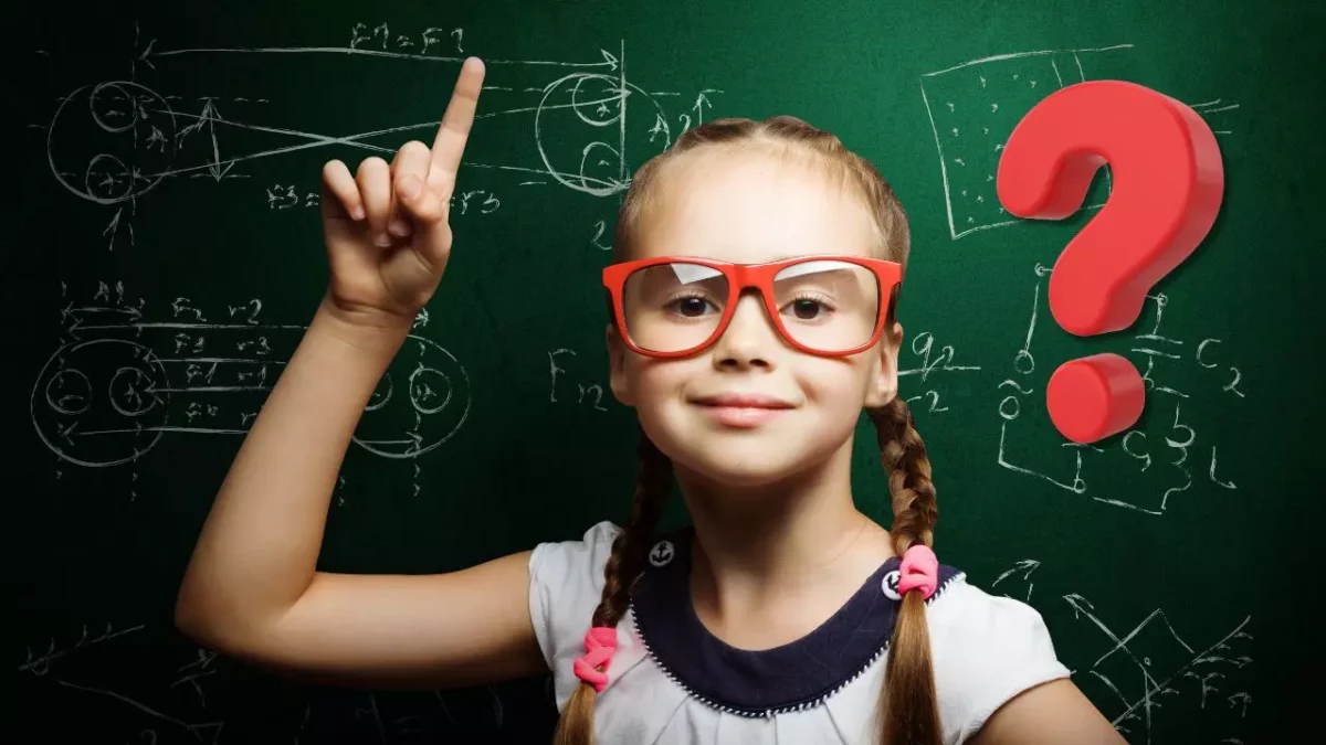 Dievčatko s červenými okuliarmi ukazuje na tabuľu s matematickými vzorcami a otáznikom na zelenej tabuli.