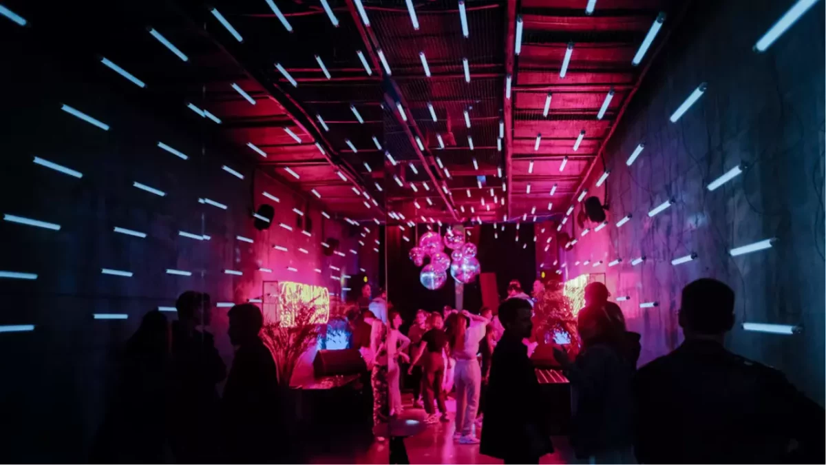 Žiarivé neonové svetlá klubu s tančiacimi ľuďmi a farebnými disko guľami na stropných lampách.