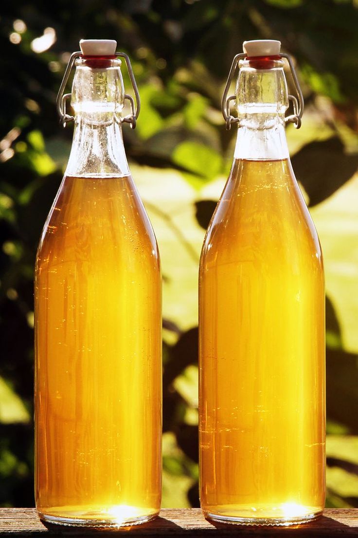 Dve fľaše zlatistého jablčného muštu na drevenom stole s rozmazaným pozadím záhrady.