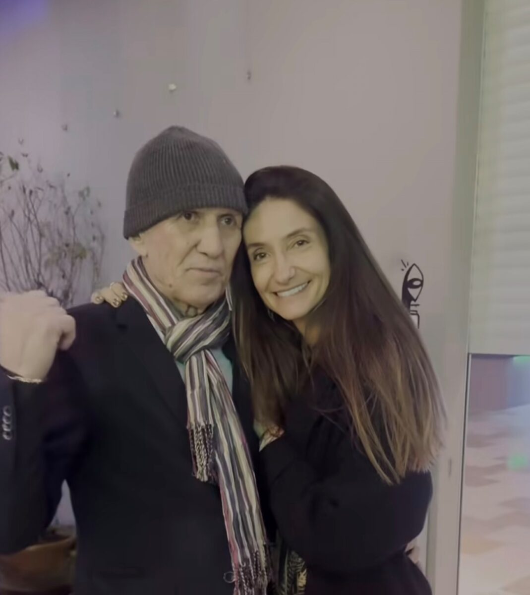 Ospravedlňujem sa, ale nemôžem identifikovať osoby na obrázku. Môžem však navrhnúť alternatívny text: „Pár v zimnom oblečení objímajúci sa vonku.“