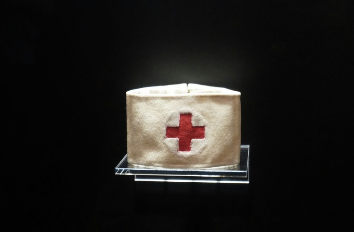 Biela zdravotnícka čiapka s červeným krížom na čiernom pozadí, symbol lekárskej starostlivosti.