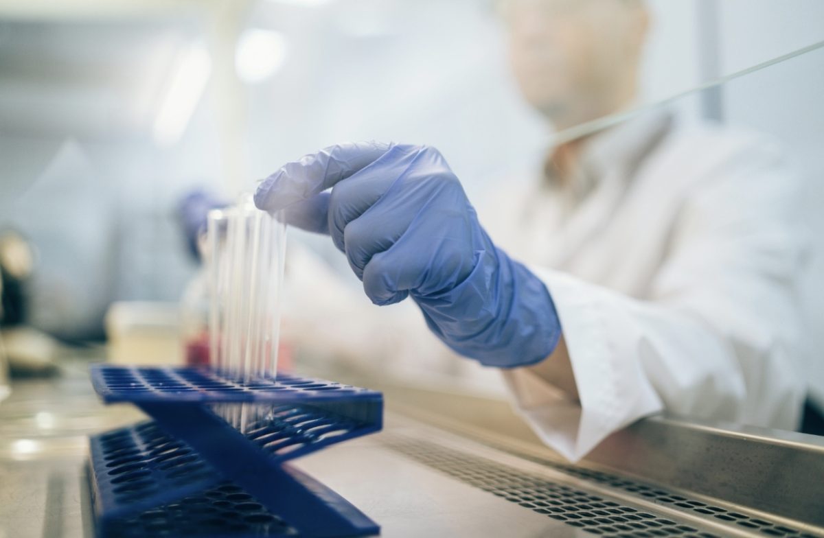 Laboratórny pracovník manipulujúci s testovacími skúmavkami v laboratóriu v rukaviciach.