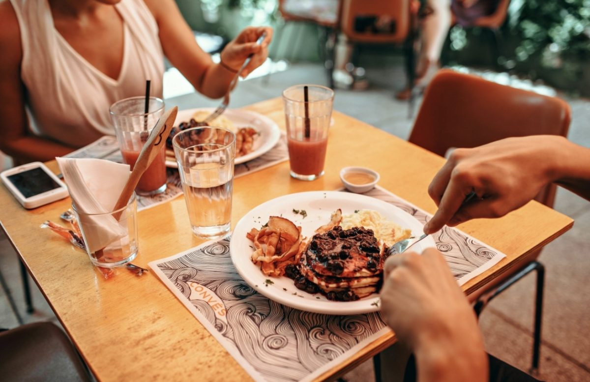 Osoby si vychutnávajú brunch s palacinkami a smoothie na terase reštaurácie.