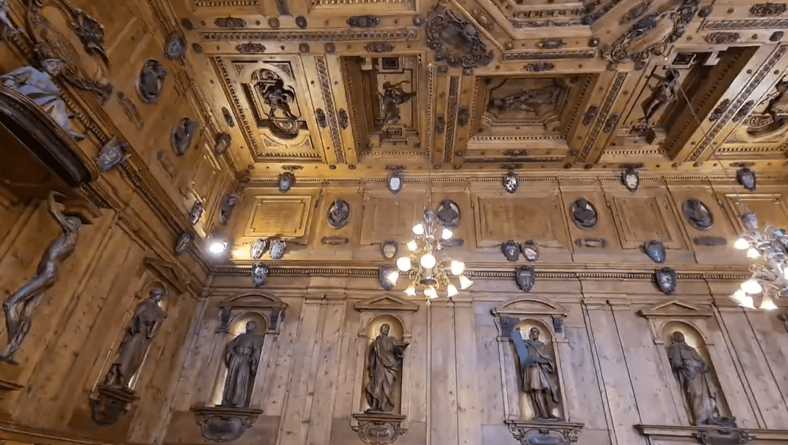 Historický drevený strop s reliéfmi a sochami svätcov, elegantné osvetlenie, interiér sochálskeho priestoru.