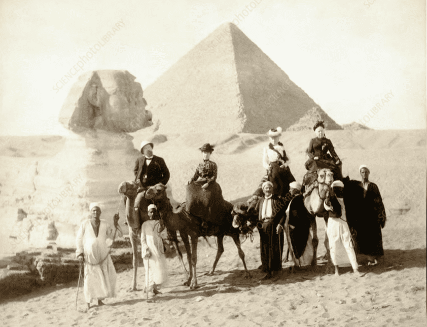 Skupina ľudí na ťavách pred Veľkou sfingou a pyramidou v Egypte, historická fotografia.
