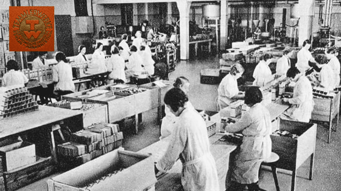Vintage továreň: Ženy v bielych plášťoch pracujú pri montážnej linke, historický pohľad na výrobu.
