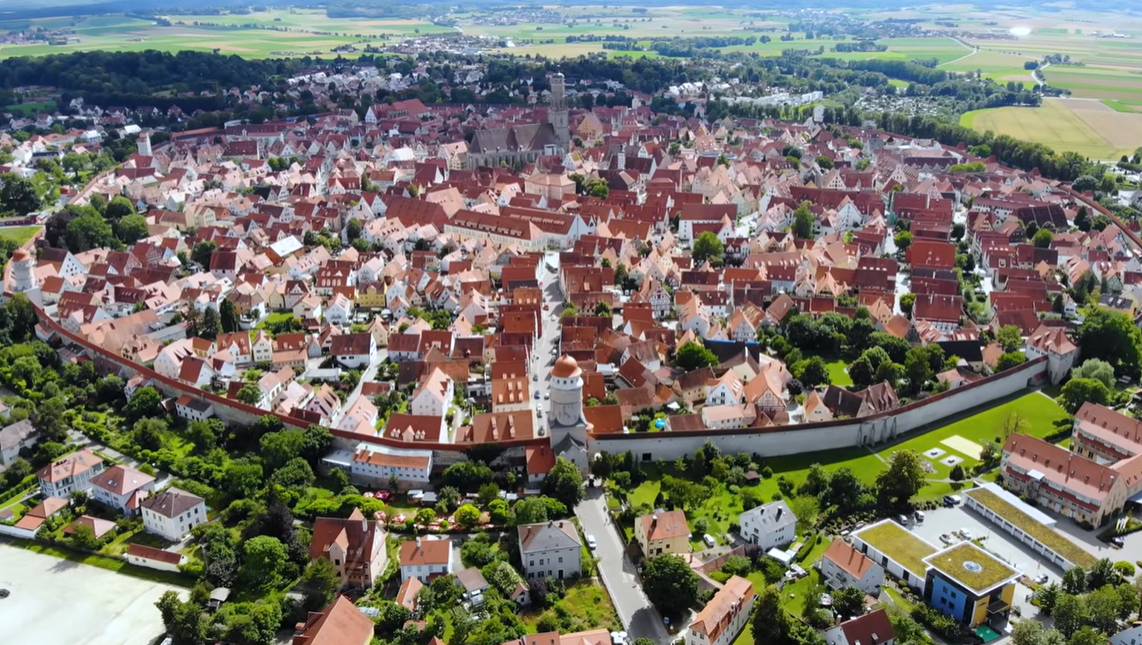 Letecký pohľad na nemecké mesto Nördlingen s historickými budovami a hradbami uprostred zelene.