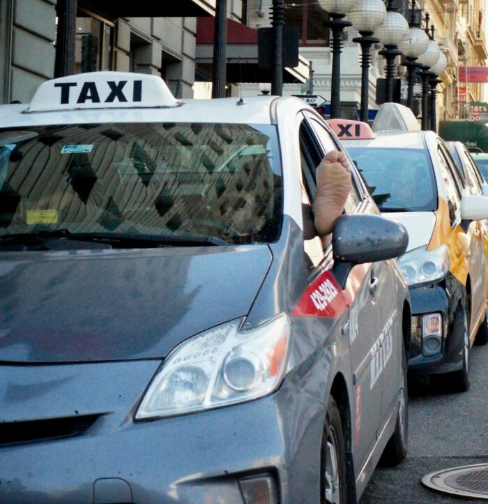 Taxi s nohou vodiča von oknom stojí na ulici v rade ďalších taxíkov.