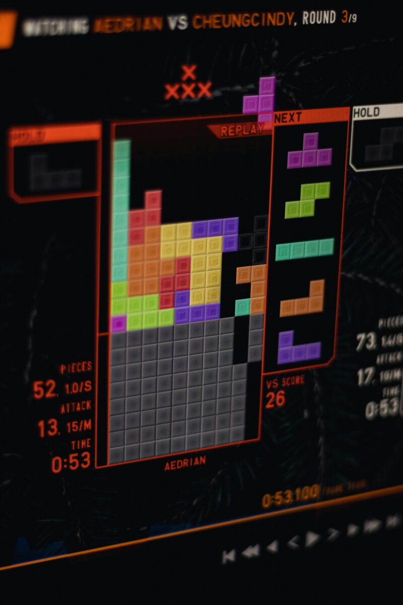 Obrázok hernej obrazovky s farebnými blokmi Tetris, čas a skóre zobrazené na obrazovke, zápas dvoch hráčov.