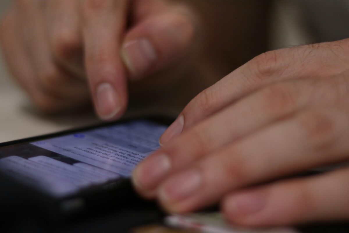 Mužská ruka píše správu na smartfóne, ukazovák sa dotýka obrazovky. Blízky pohľad na prsty a mobilný telefón.