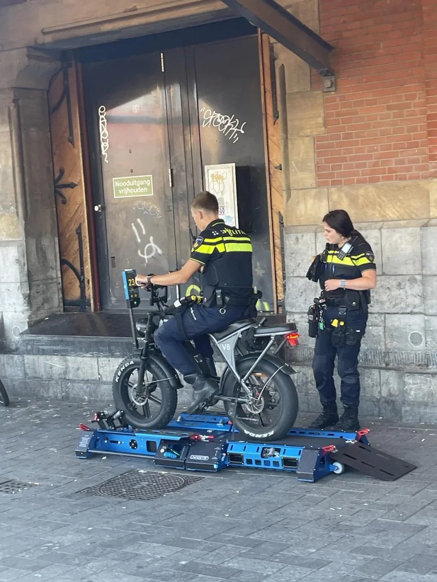 Policajti kontrolujú elektrický bicykel na mobilnej váhe pred budovou so zamknutými dverami.