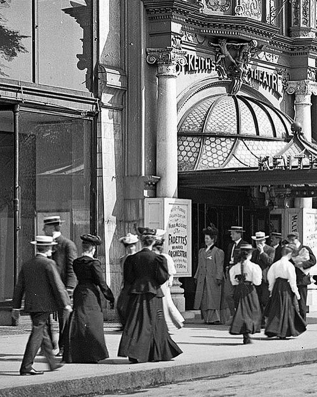 História: Ľudia v staromódnom oblečení prechádzajú okolo historického divadla Keith's Theatre.