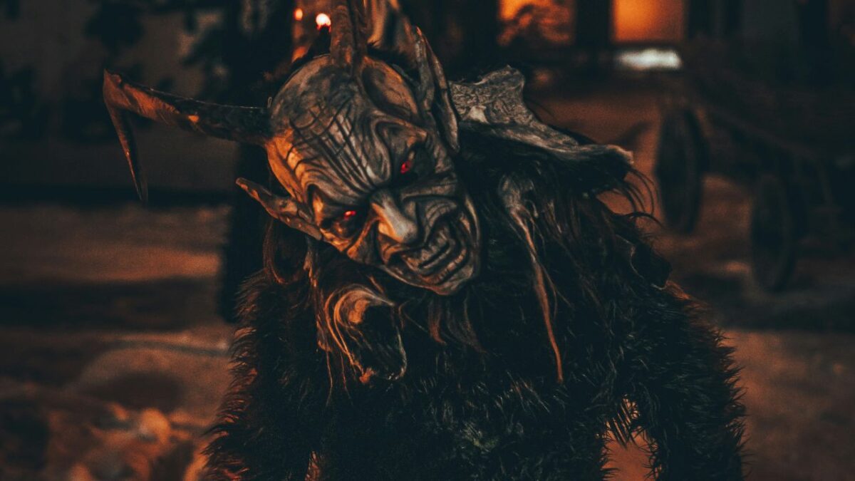 Krampus v tradičnom kostýme s červenými očami počas nočnej zimnej slávnosti.
