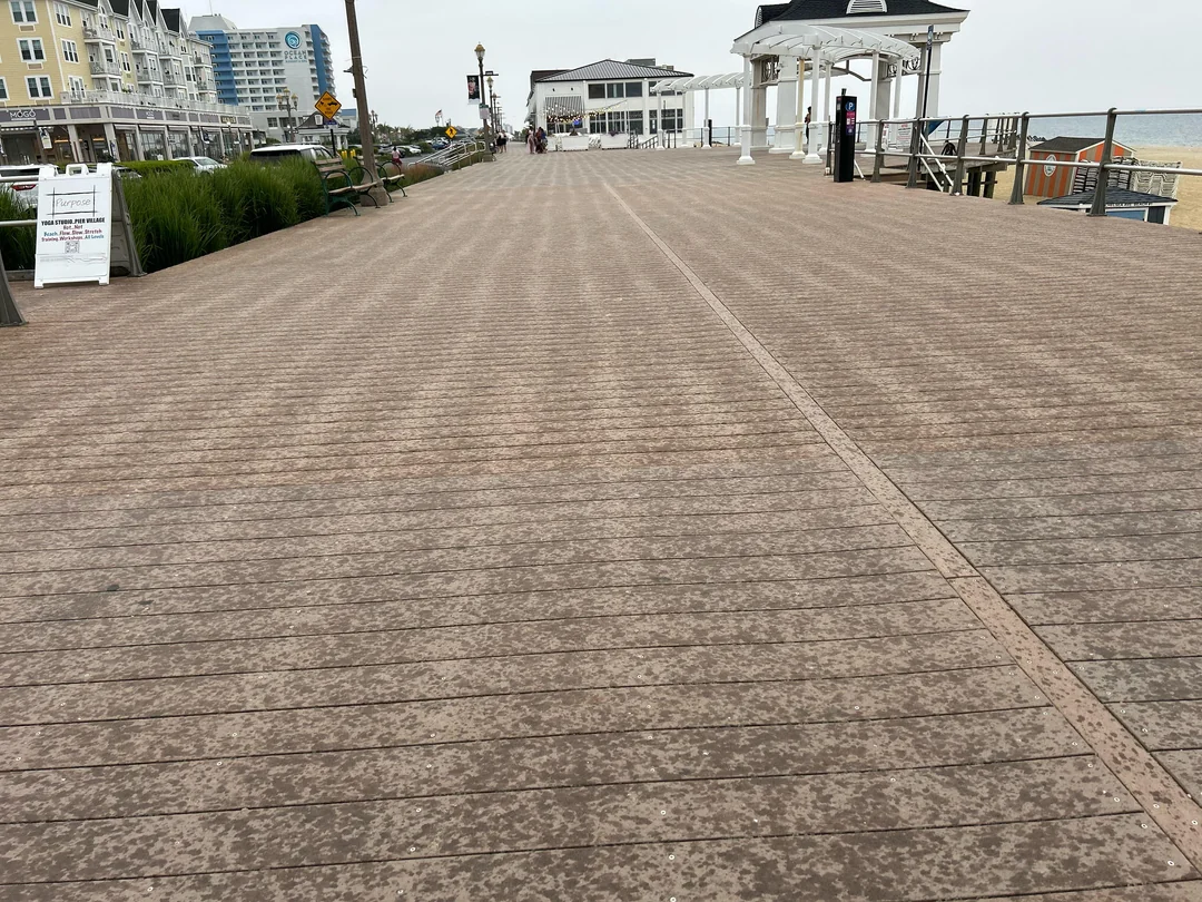Promenáda pri pláži s drevenou podlahou, pozdĺž ktorej sú obchody a altánok s výhľadom na more za oblačného počasia.