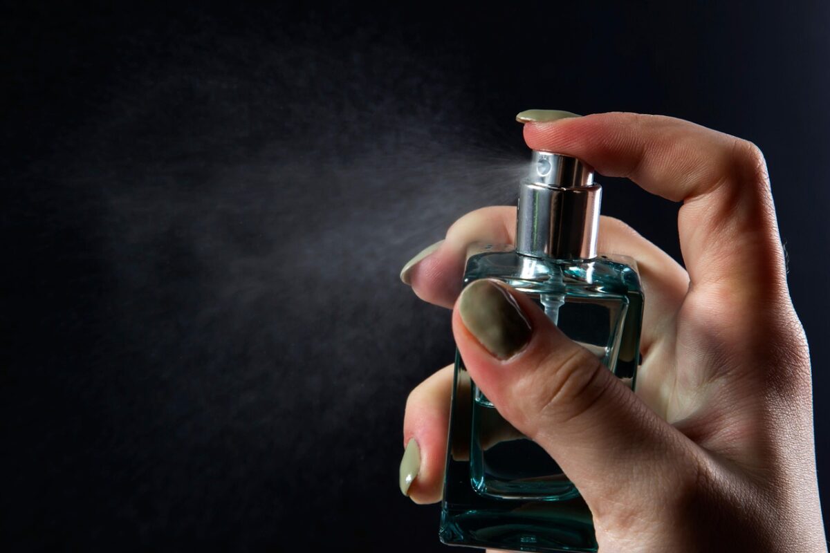Osoba strieka parfum z fľaštičky v tmavom prostredí. Jemná hmla vytvára elegantný efekt.
