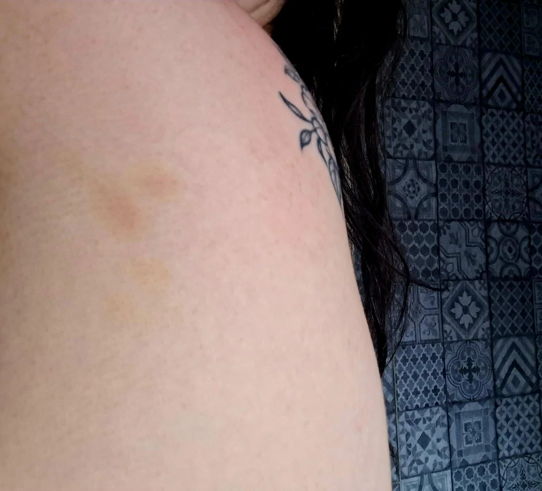 Tetovanie na ramene s jednoduchým vzorom, tmavé vlasy, kachličkový vzor na pozadí.
