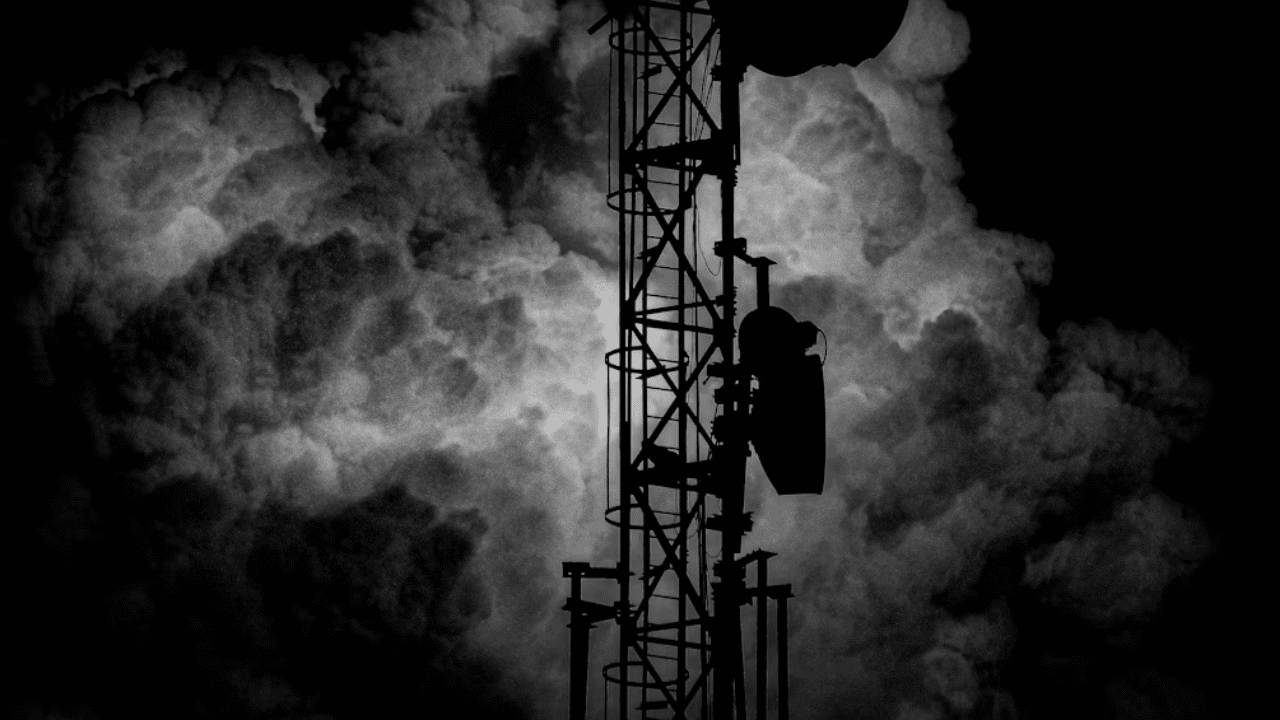 Telekomunikačná veža v tmavom prostredí, obklopená dramatickými oblakmi na nočnej oblohe.