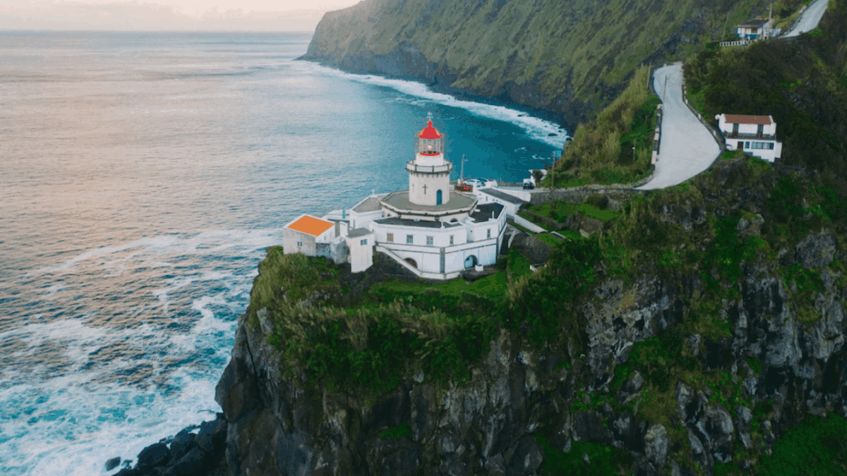 Maják na útesoch s výhľadom na oceán a zelené hory, nádherná scenéria pre cestovateľov.