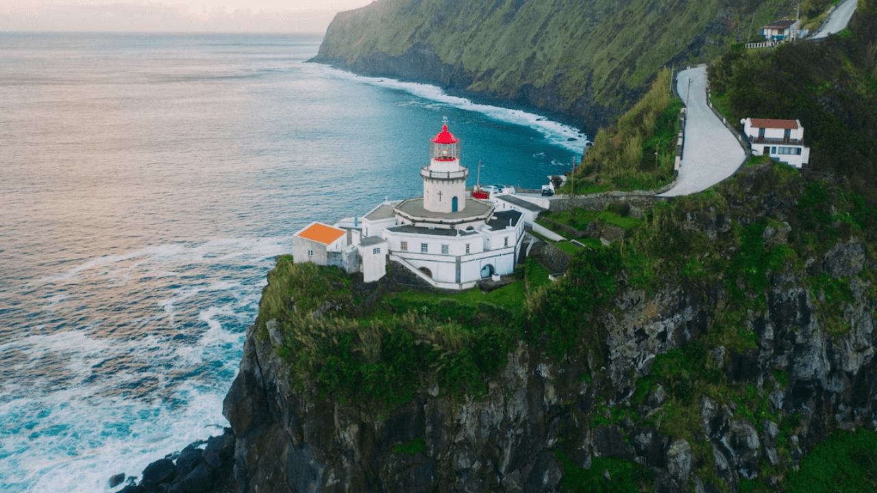 Maják na útesoch s výhľadom na oceán a zelené hory, nádherná scenéria pre cestovateľov.