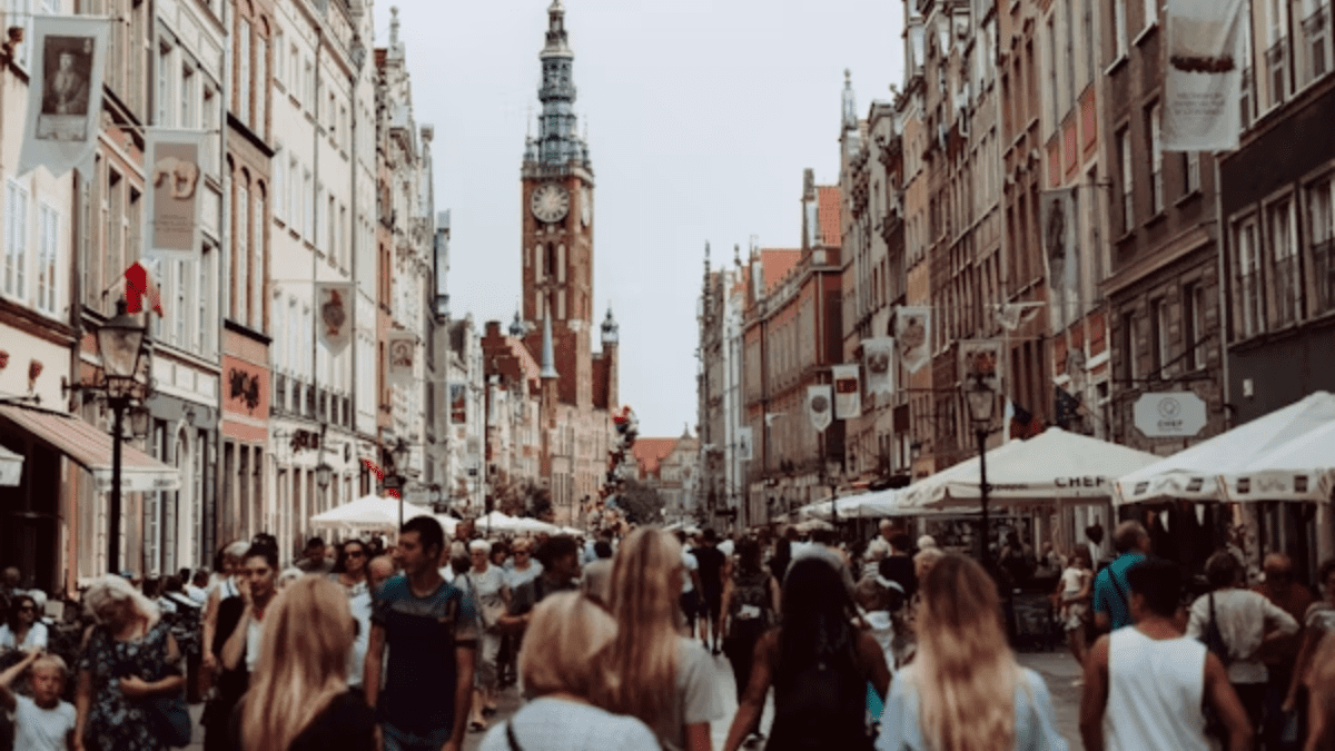 Historická ulica plná turistov so starobylou vežou v pozadí na slnečný deň.
