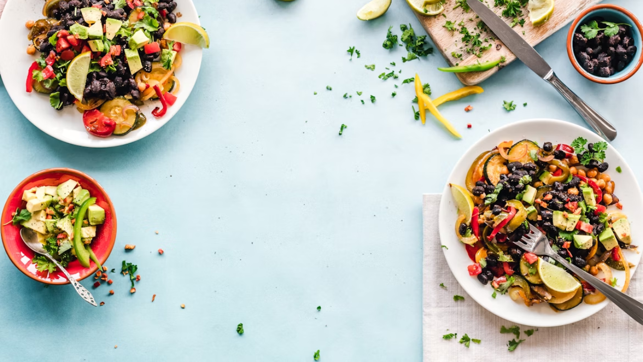 Farebné vegetariánske jedlo na svetlom stole s avokádom, limetkou a koriandrom, podávané na tanieroch.