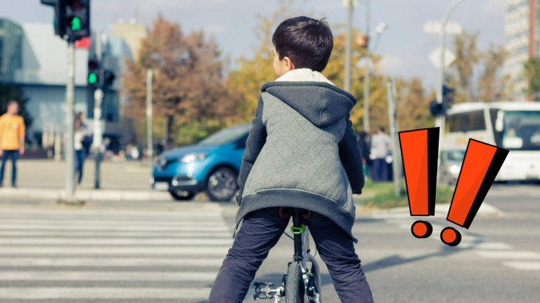 Chlapec na bicykli na prechode pre chodcov pri zelenom semafore s autami v pozadí.