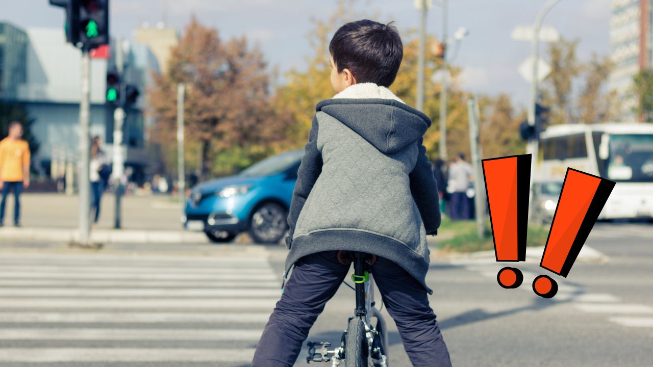 Chlapec na bicykli na prechode pre chodcov pri zelenom semafore s autami v pozadí.
