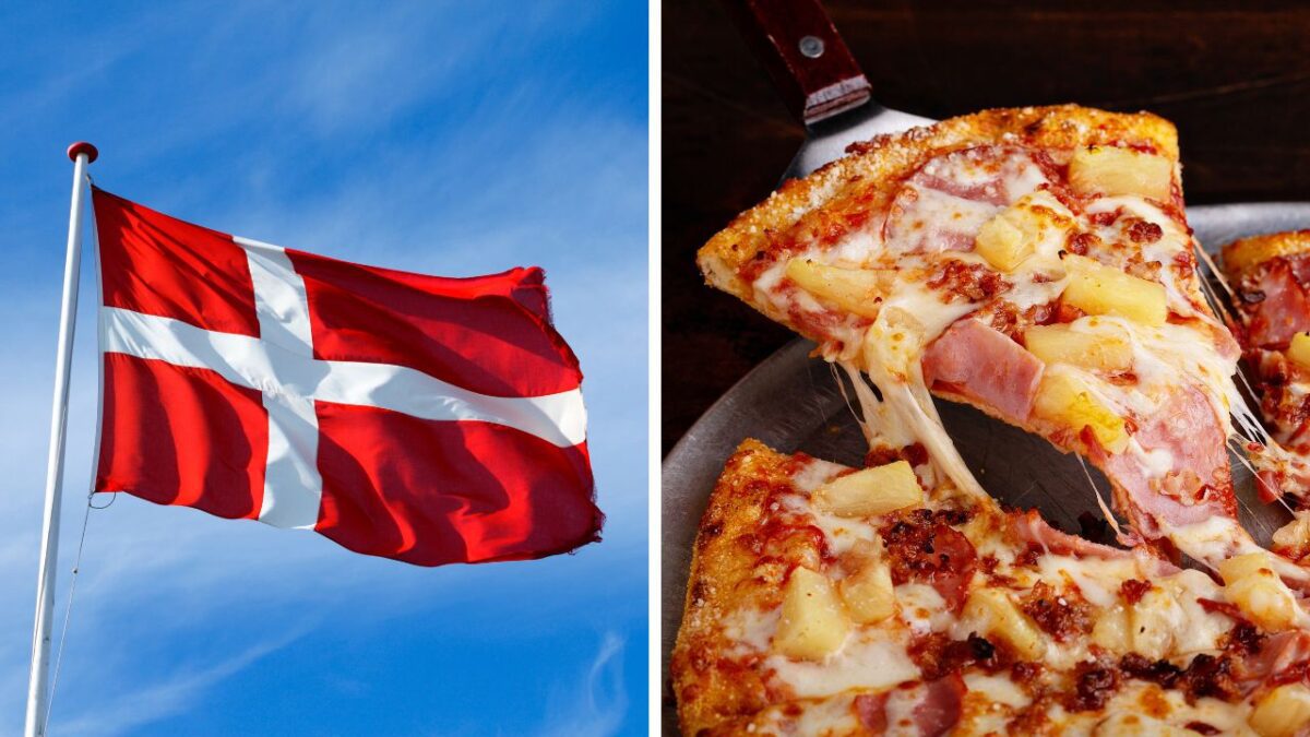 Dánska vlajka vo vetre a hawajská pizza s ananásom a šunkou na tanieri.