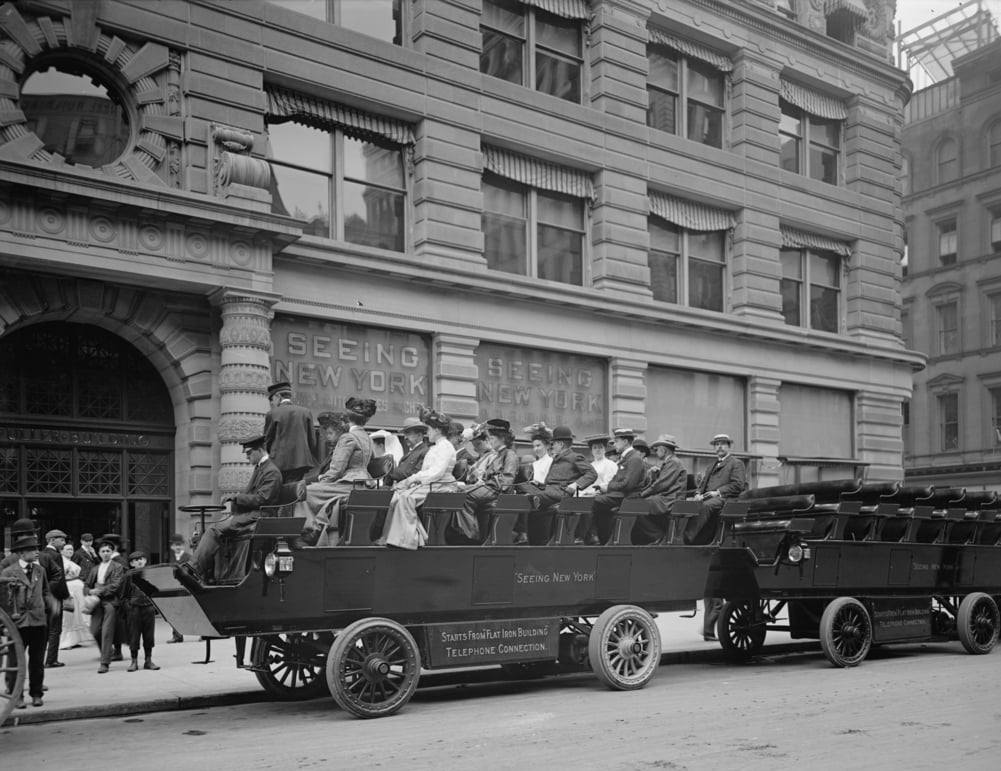 Historický panoramatický autobus plný cestujúcich na prehliadke mesta pred budovou v New Yorku, začiatkom 20. storočia.